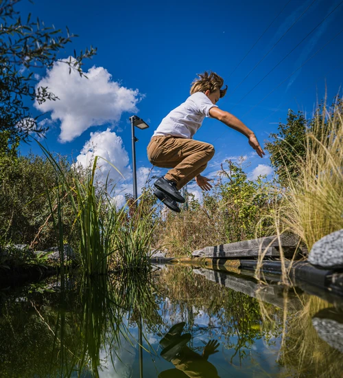Ein Junge springt im Au&szlig;enbereich der KLIMA ARENA &uuml;ber eine Wasserfl&auml;che.