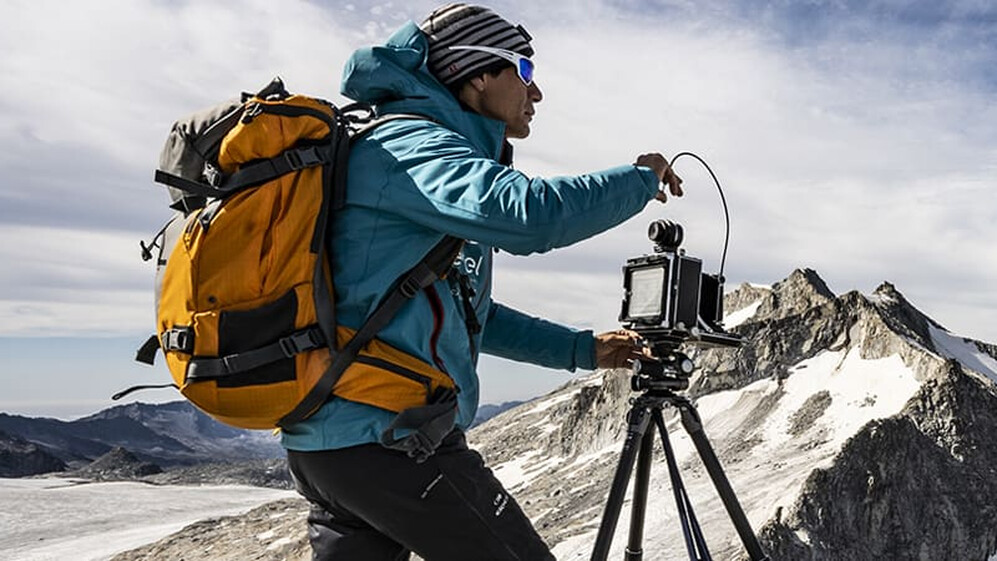 Fotograf mit Ausr&uuml;stung und Stativ beim Fotografieren eines Gletschers.