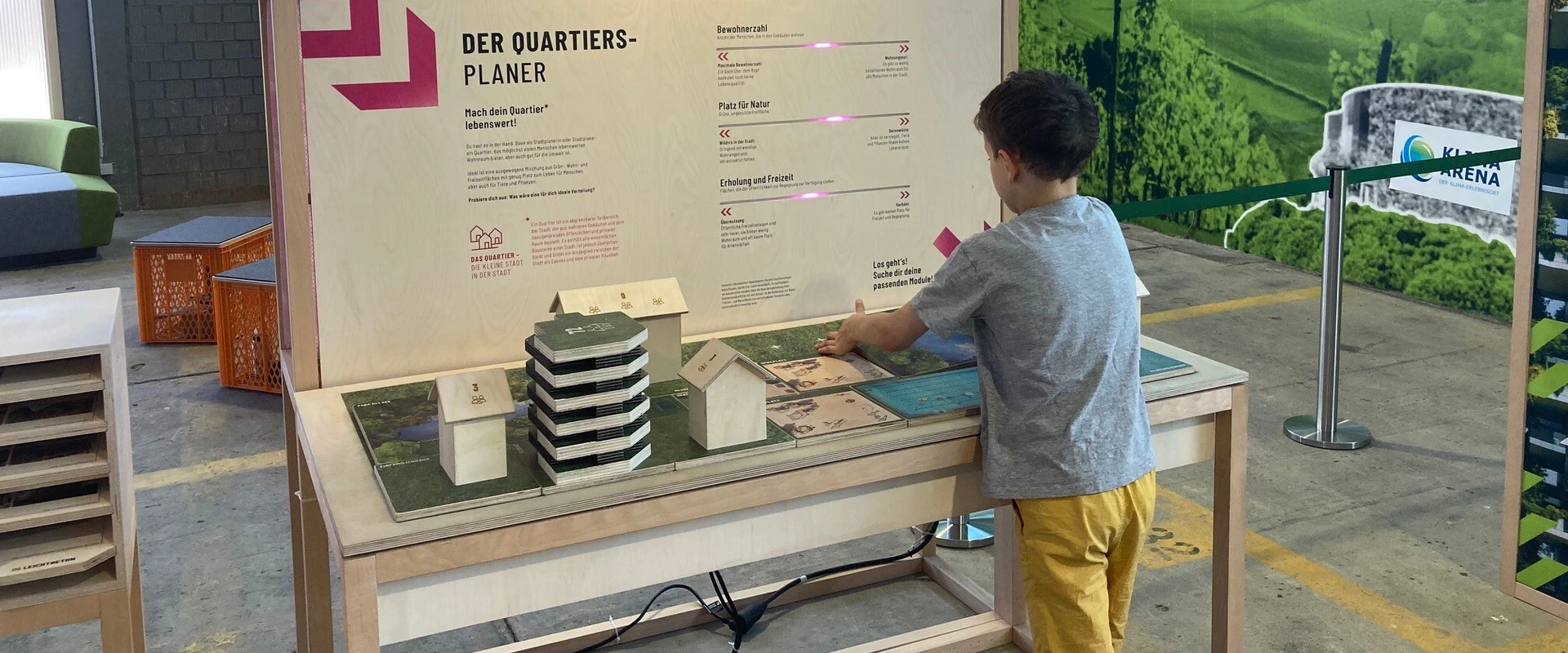 Ein Kind spielt mit Baukl&ouml;tzen an einem Exponat zur Fl&auml;chennutzung in der Stadt.