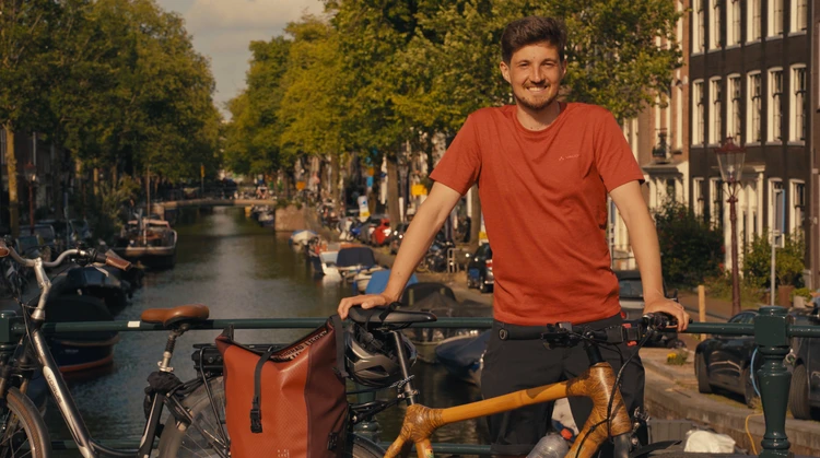 Ein Mannsteht lachend mit seinem Fahhrad auf einer Grachtenbr&uuml;cke in Amsterdem.